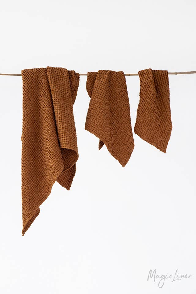Burnt orange waffle linen-cotton blend bath towels, three pieces of the set hanging together on a natural rod.