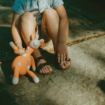 
                    
                      Curious Plush Giraffe, orange crochet knit plush toy with white spots, held in a child's hand for scale.
                    
                  