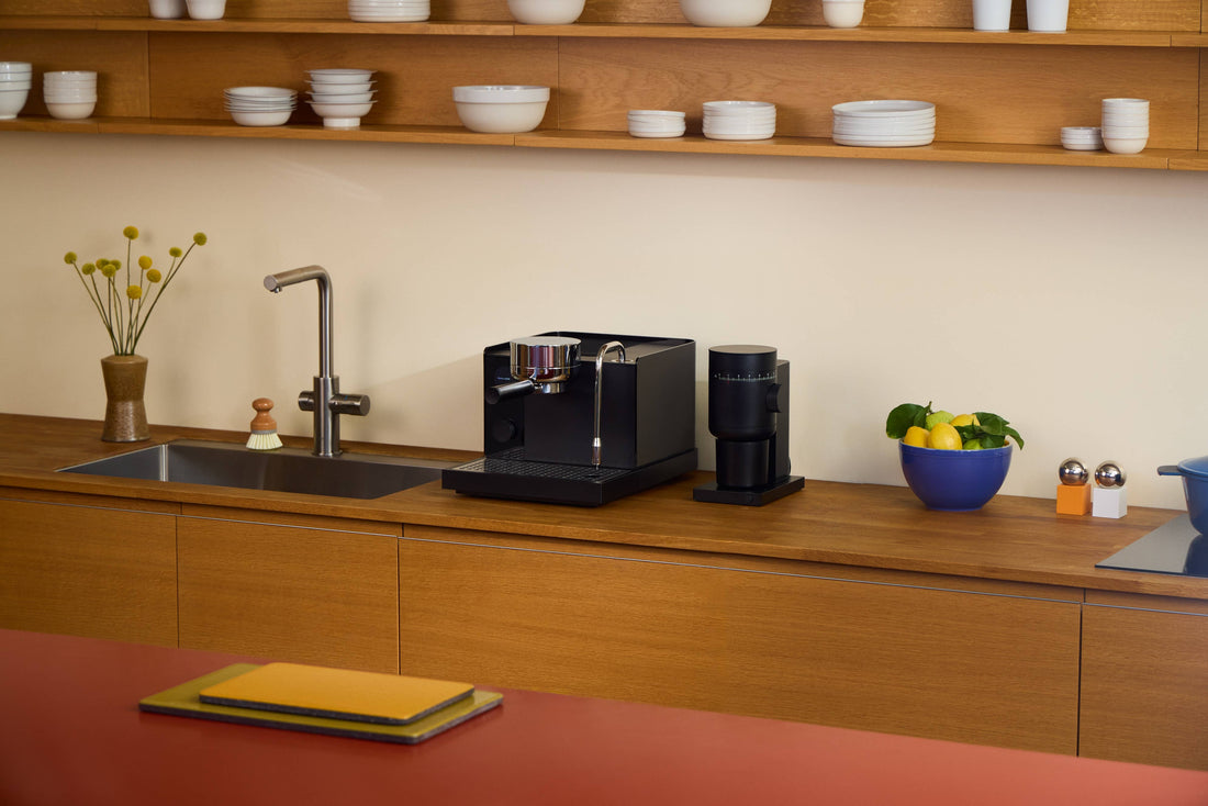 Black Fellow Opus 2 conical burr grinder on a wooden kitchen counter, next to a black espresso machine.