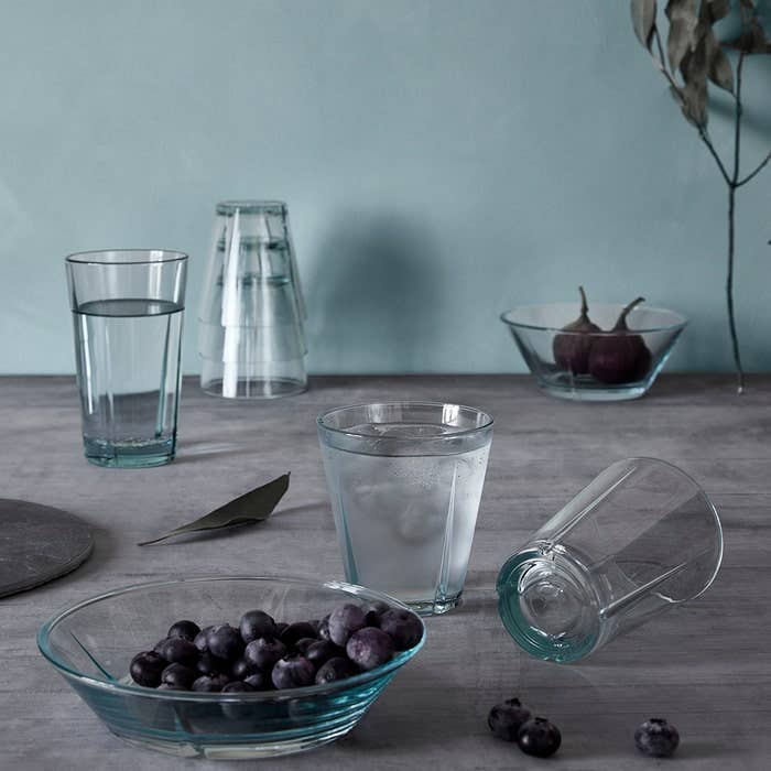 Multiple Grand Cru recycled glass tumblers, clear with subtle blue-green tint, some upright with water, one stacked, one…