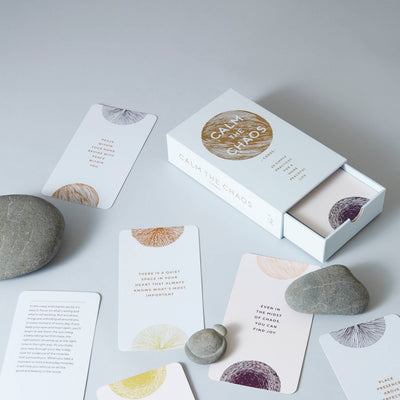 
                    
                      Calm The Chaos Cards mindfulness deck, open white box, gold title, fanned out cards with colorful patterns, text, flat lay.
                    
                  