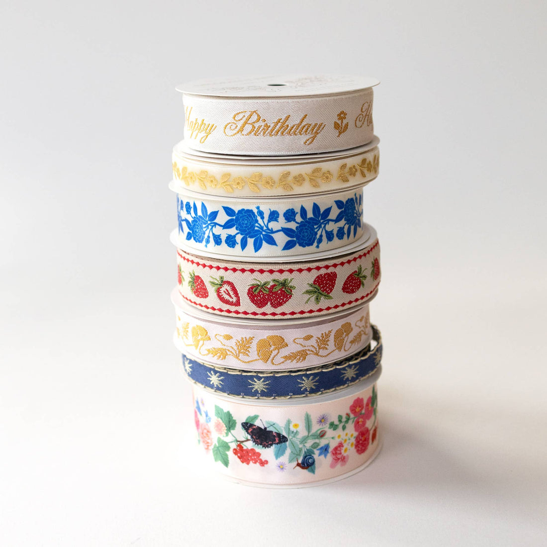 Stars embroidered ribbon (dark blue with white stars) at base of stacked spools of varied designs, including red strawberry…