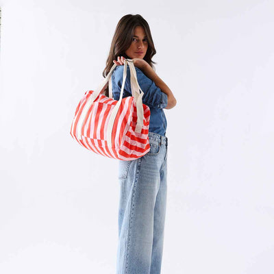 
                    
                      Raphael diaper bag, red and pink striped cotton, carried on model's shoulder, side view.
                    
                  