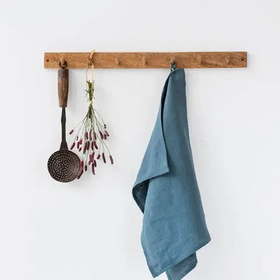
                    
                      Blue-green linen tea towel, folded and draped over a wooden hook, highlighting its natural texture.
                    
                  