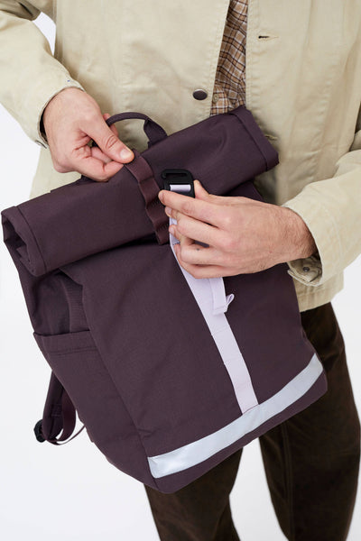 
                    
                      Lars Roll Backpack, wine RIPSTOP fabric, hands securing the roll-top closure with a black buckle and light grey reflective…
                    
                  
