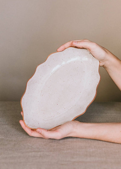 
                    
                      Handcrafted Stoneware Tray, speckled cream with reddish-brown wavy rim, held in hands for scale.
                    
                  