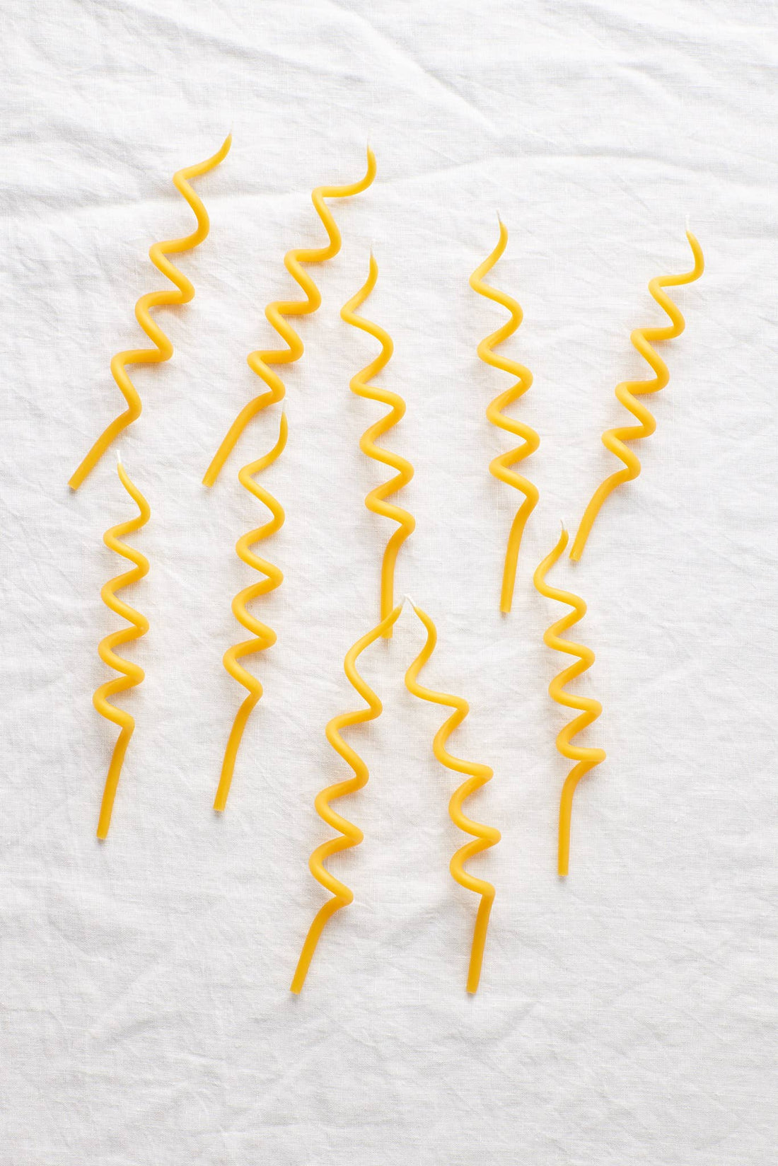 Twirl beeswax birthday candles, yellow spiral shape, scattered flat lay arrangement on white fabric.