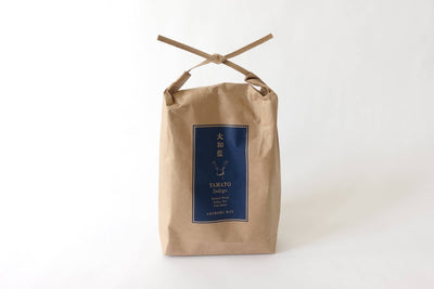 
                    
                      Curious Corners Yamato Indigo Shibori Kit, in a tied kraft paper bag with indigo blue label, full front view on white…
                    
                  
