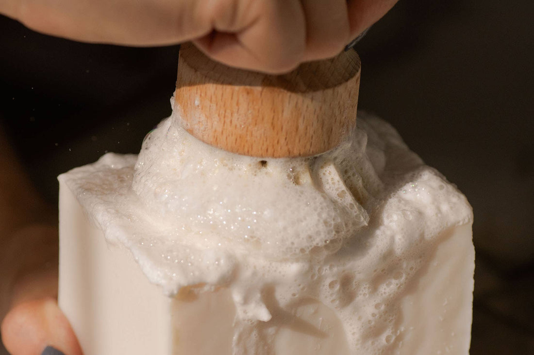 Dish Block Solid Dish Soap, white, actively lathering with a natural wooden dish brush, close-up of thick foam.