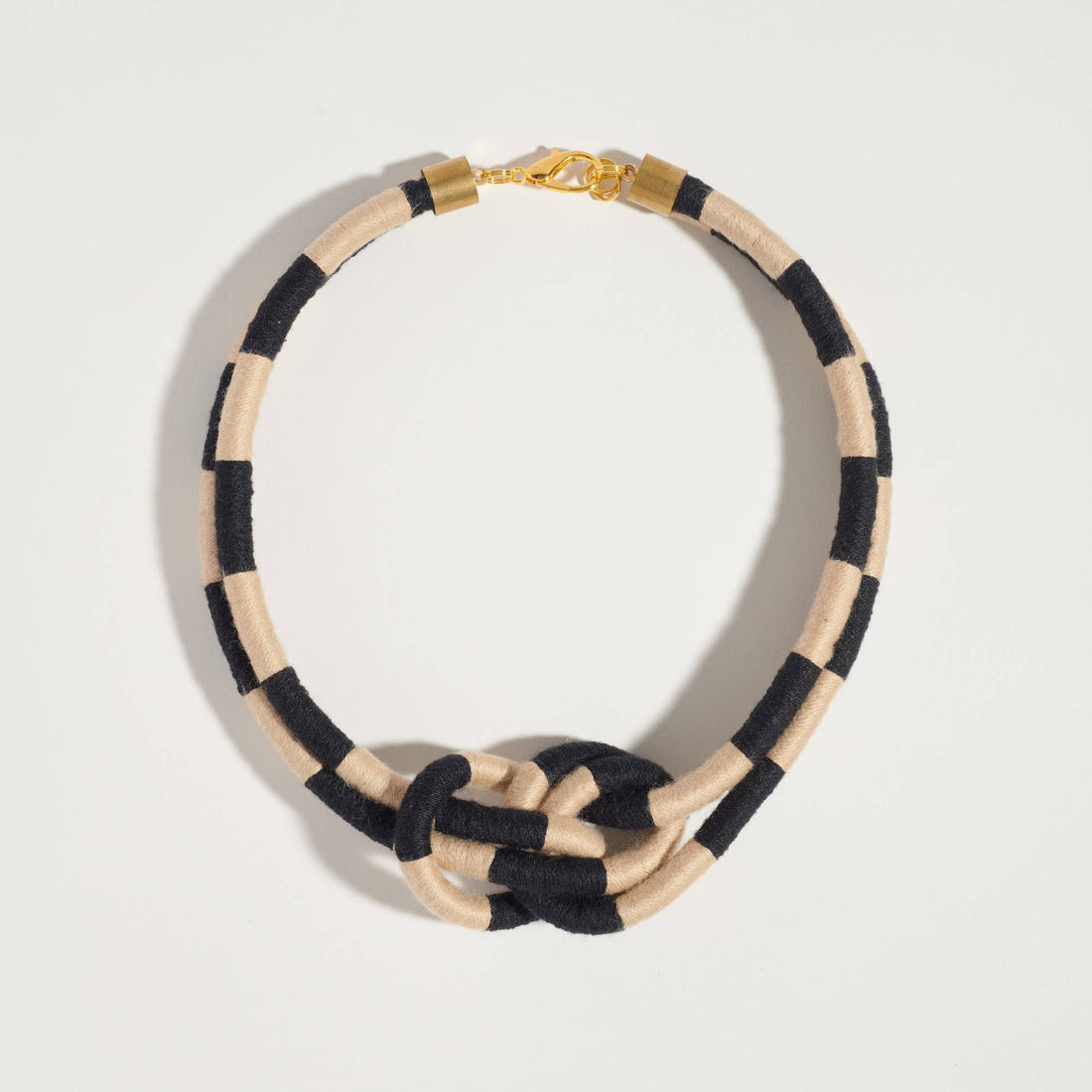 Sasha Checkered Double Dragon necklace, black and beige checkered textile, brass clasp, flat lay on white.
