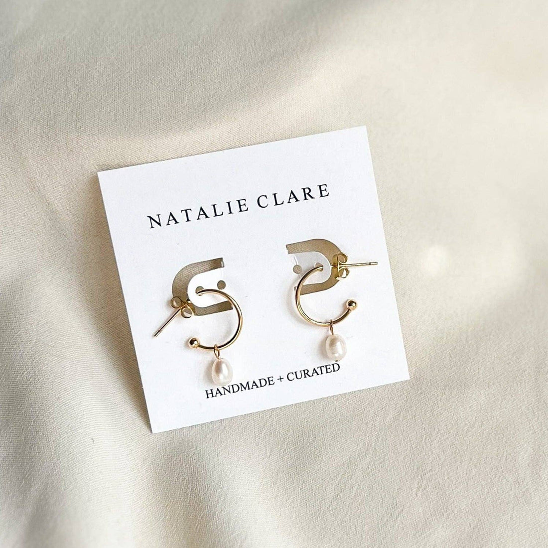 Natalie Clare Chloe Pearl Earrings, 18K gold-plated brass with white pearl drops, flat lay pair on brand card showing posts.