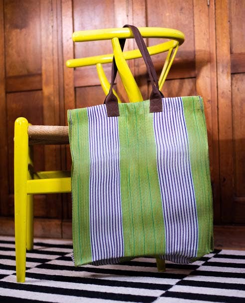British Colour Standard Woven Market Tote, green, white, and dark striped woven fabric, brown webbing handles, leaning on a…