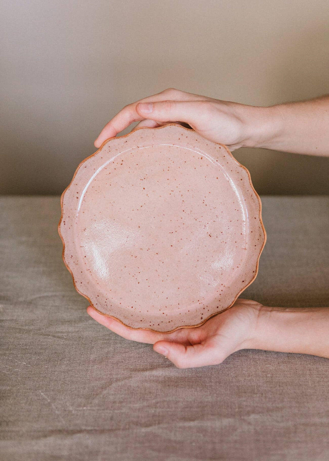 Ohyoko Ceramics Handcrafted Stoneware Plate, speckled blush pink, high-fired stoneware with scalloped brown rim, held by…