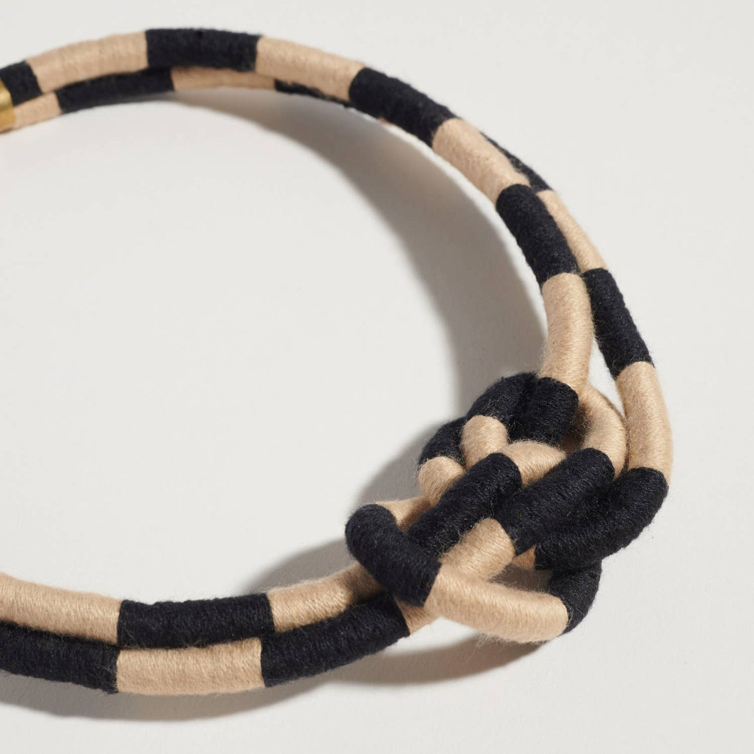 Checkered Double Dragon necklace, black and beige woven textile, close-up of central knot and checkerboard pattern.