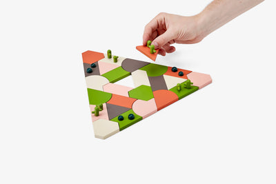
                    
                      Areaware Blockitecture Desert Garden building blocks, hand placing green cactus piece on wood desert landscape, top view.
                    
                  