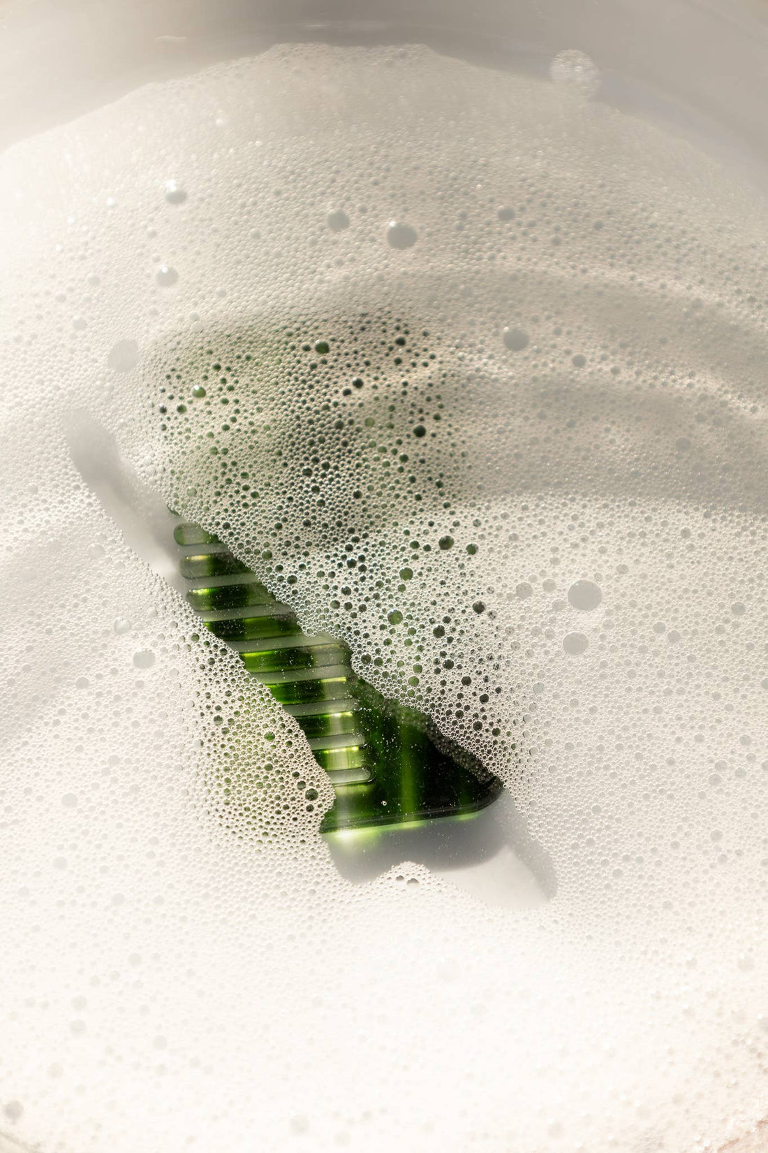 Travel Wide-Tooth Wave Comb, emerald translucent cellulose acetate, partially covered by white frothy bubbles.