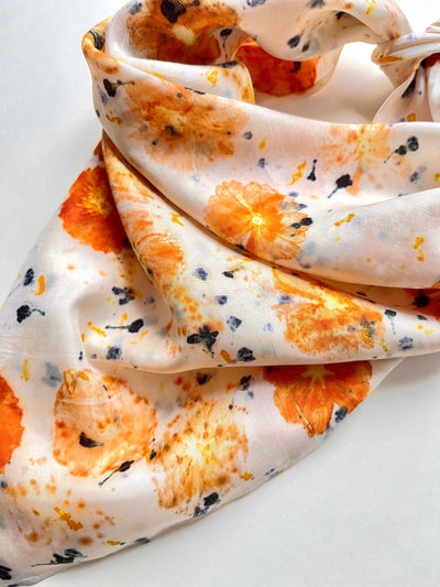 
                    
                      Abby silk habotai bandana scarf, draped close-up showing vibrant orange floral imprints and dark blue specks on creamy…
                    
                  