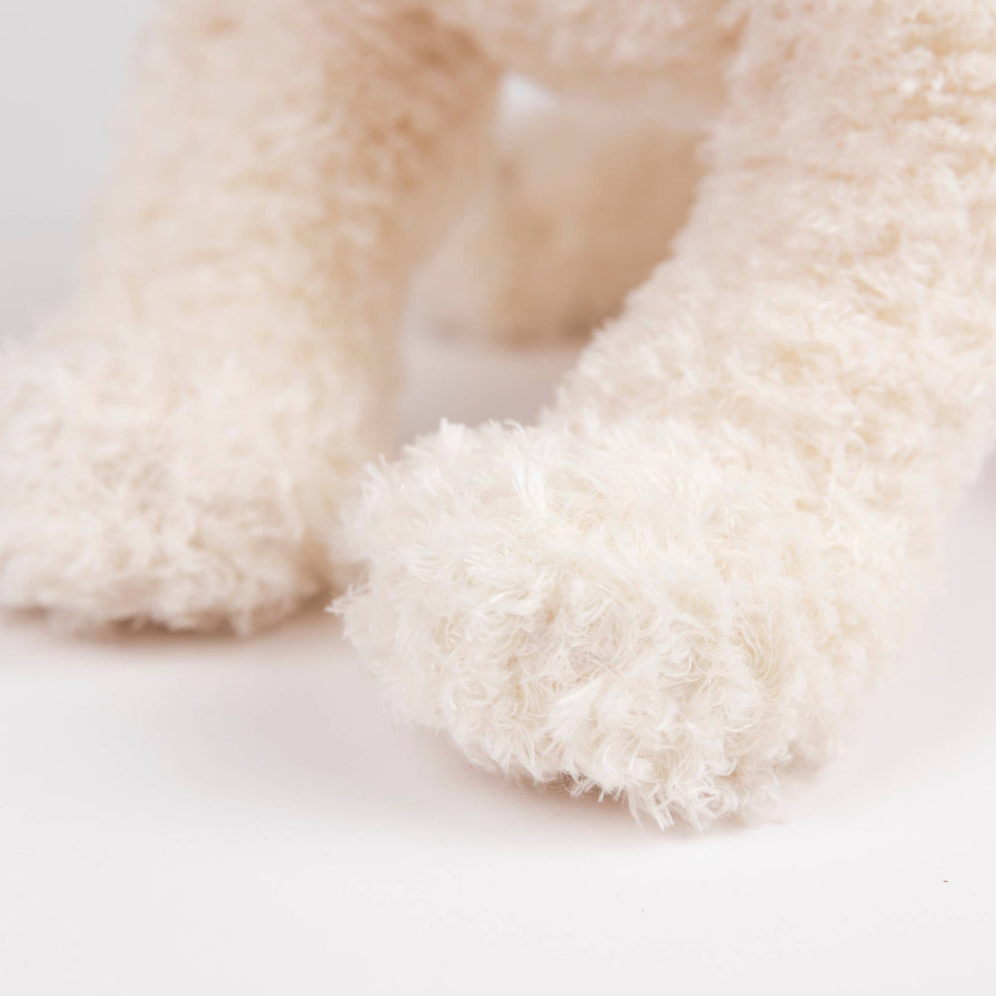 Eliot Stuffed Dog, creamy white plush paws close-up, focusing on the soft polyester material texture.