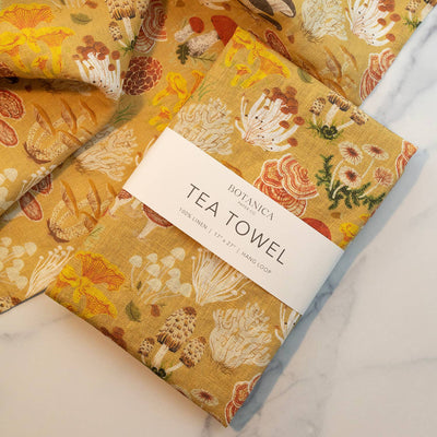 
                    
                      Botanica Paper Co. Mushrooms 100% linen tea towel, mustard yellow with colorful mushroom print, folded with brand band…
                    
                  