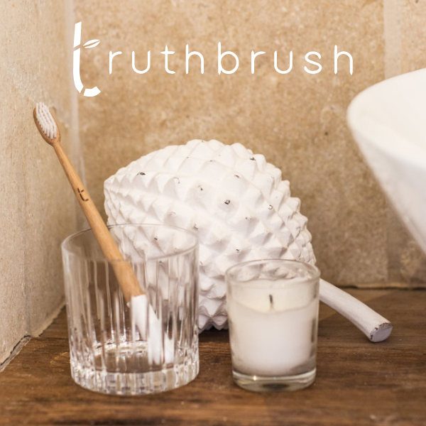 Cloud White Bamboo Toothbrush, natural bamboo handle and white bristles, standing in a ribbed glass on a wooden bathroom…