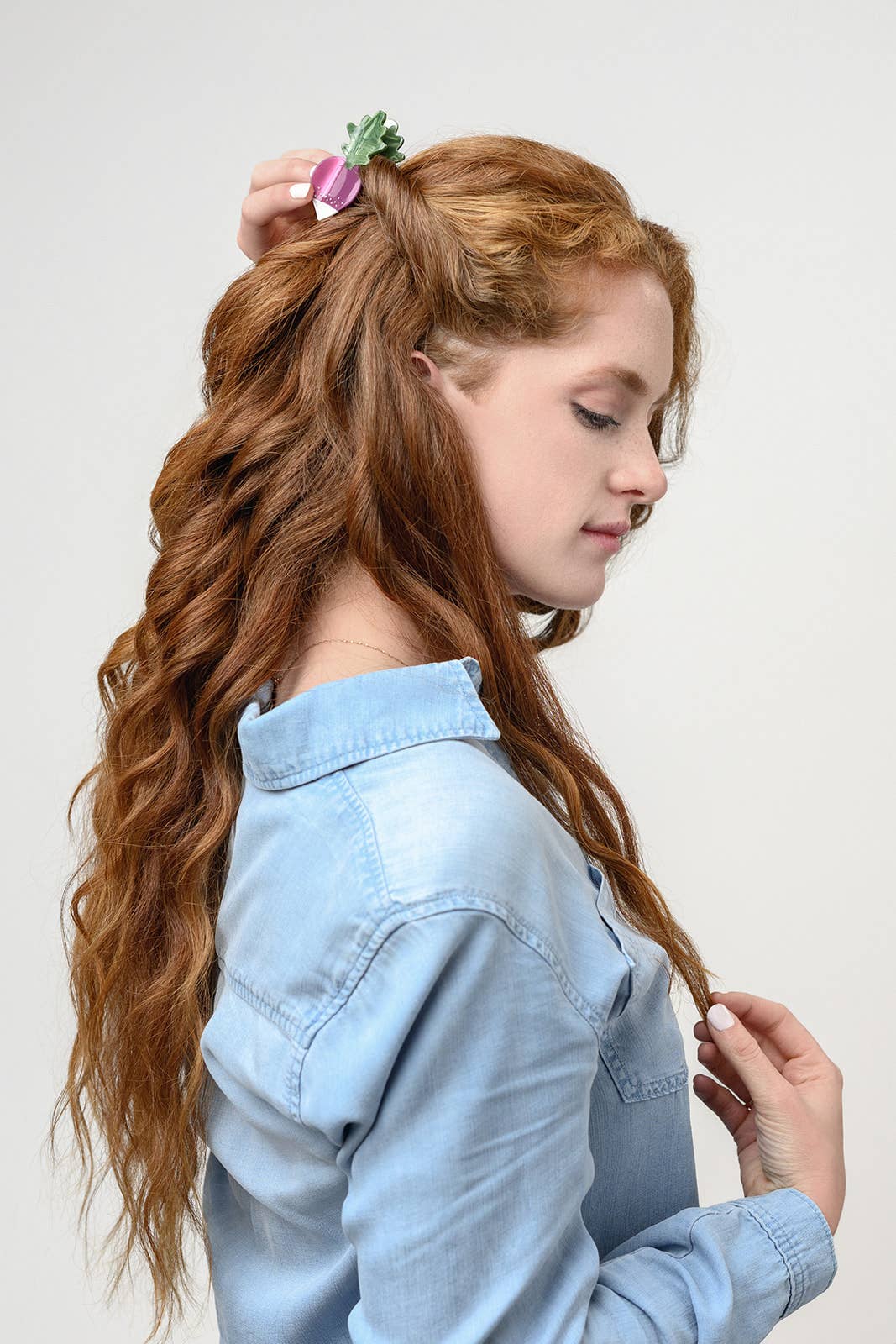 French Radish hair clip, pink and green cellulose acetate with rhinestones, styled in a model's wavy hair, side profile.