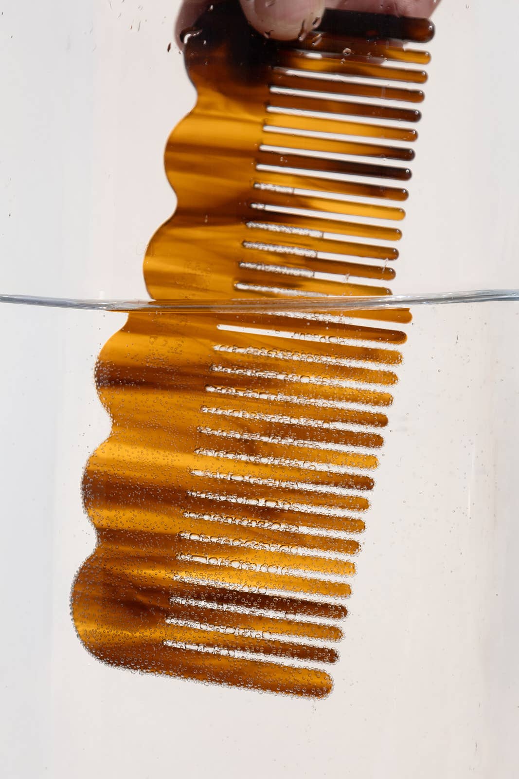 Signature Wide-Tooth Wave Comb, rich ebony plant-based cellulose acetate, half submerged in water with fine bubbles,…