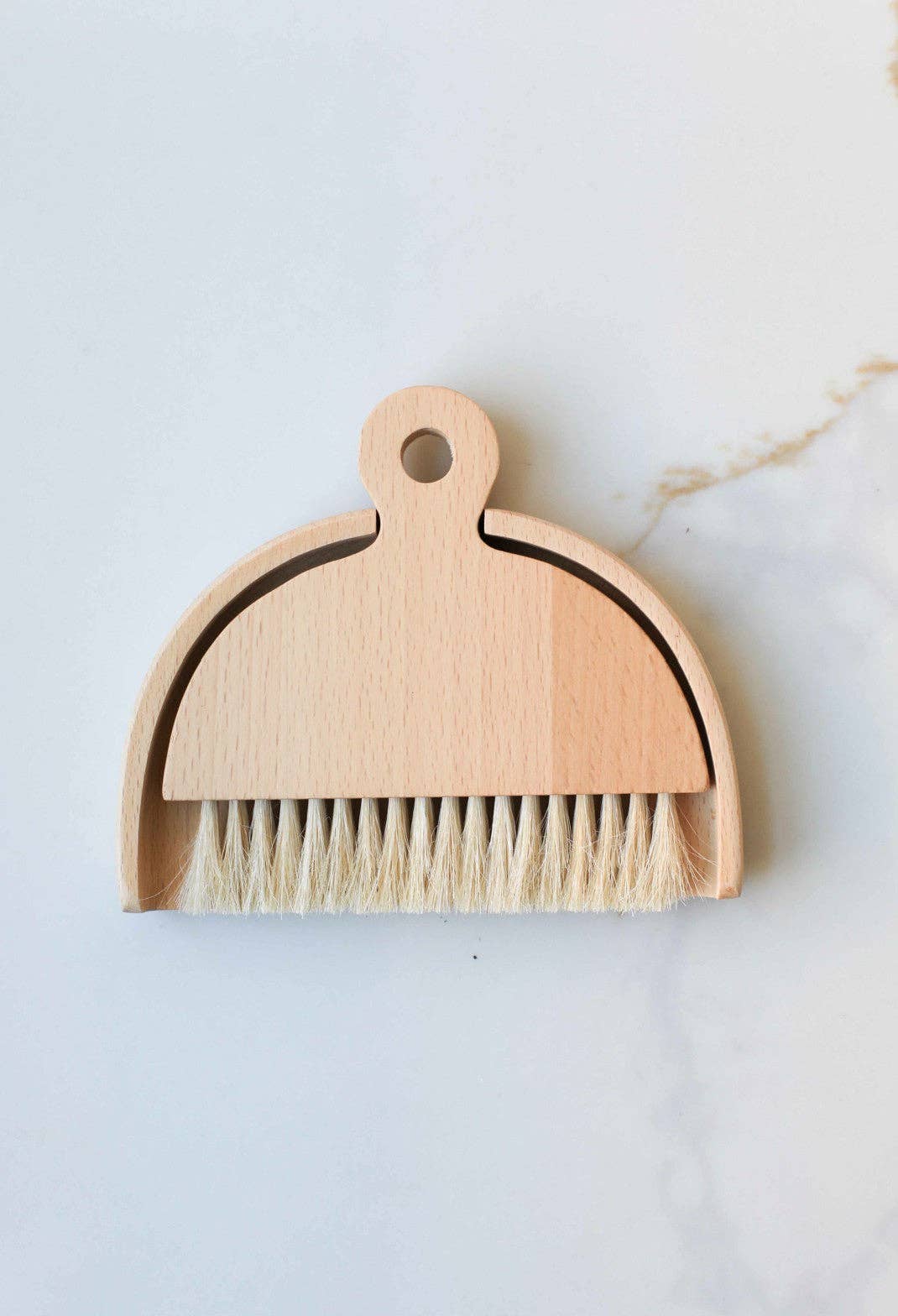 Table Brush with light wood dustpan and natural sisal bristles, nested together, flat lay on white marble.