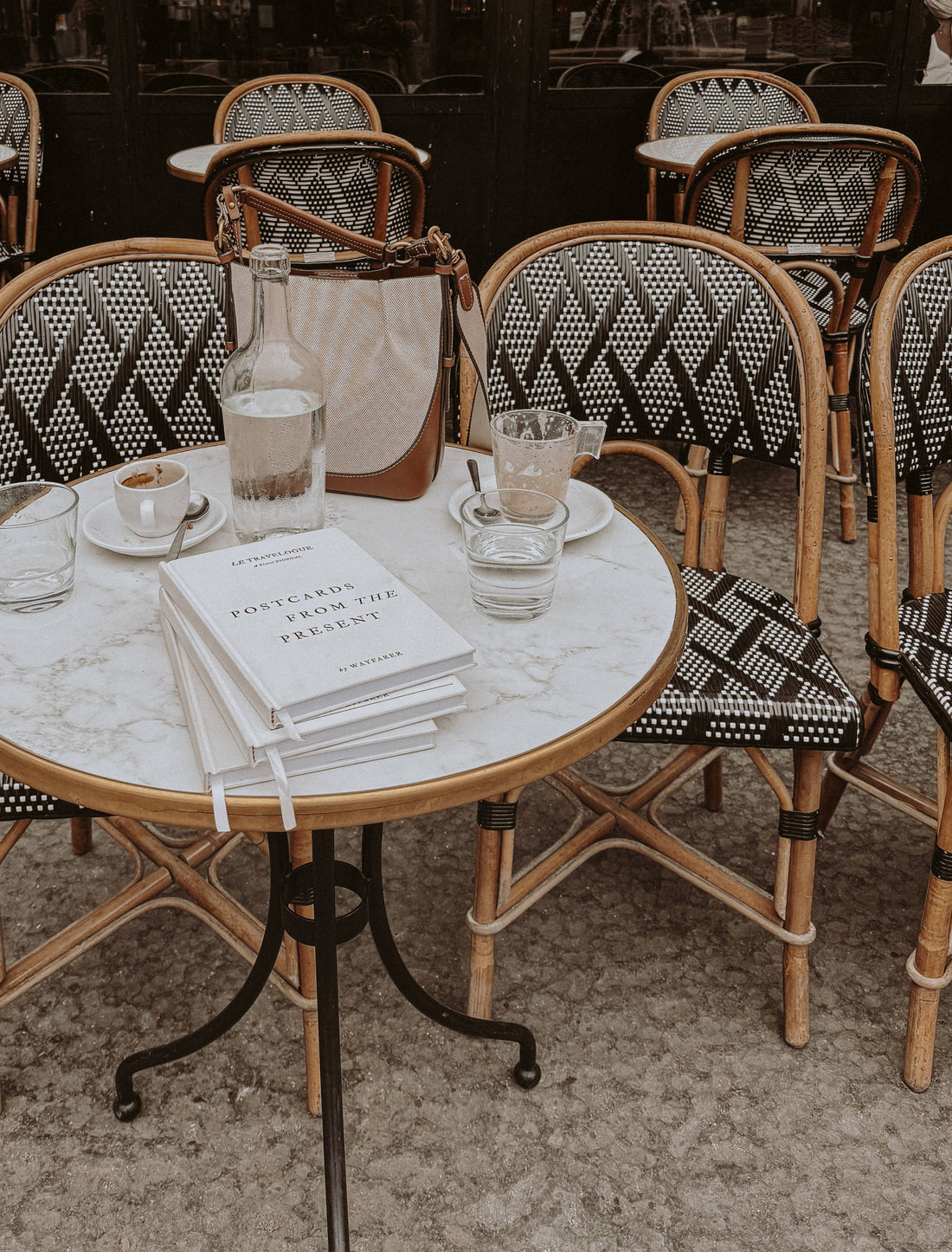 Wayfarer Postcards from the Present Travel Journal, white linen cover, stacked on marble cafe table with coffee.