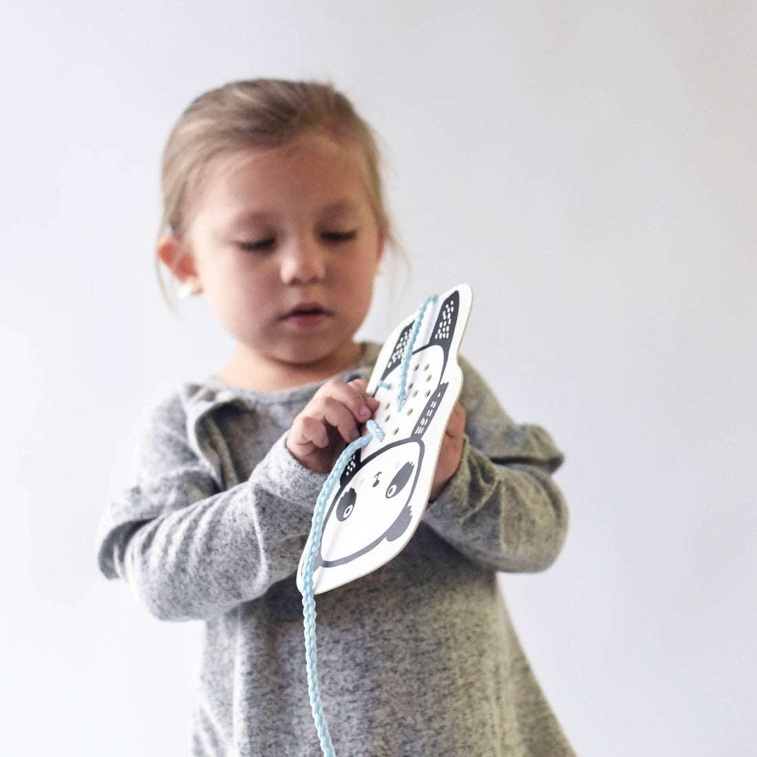 Baby Animals lacing card, black and white panda design, child's hands actively threading a blue fabric lace, close-up.