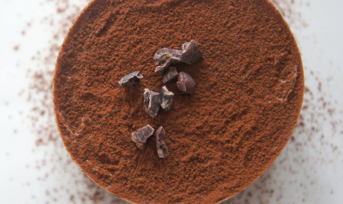 Nib + Noble Organic Dark Drinking Chocolate mix, texture close-up of deep brown cocoa powder with irregular cocoa nibs.