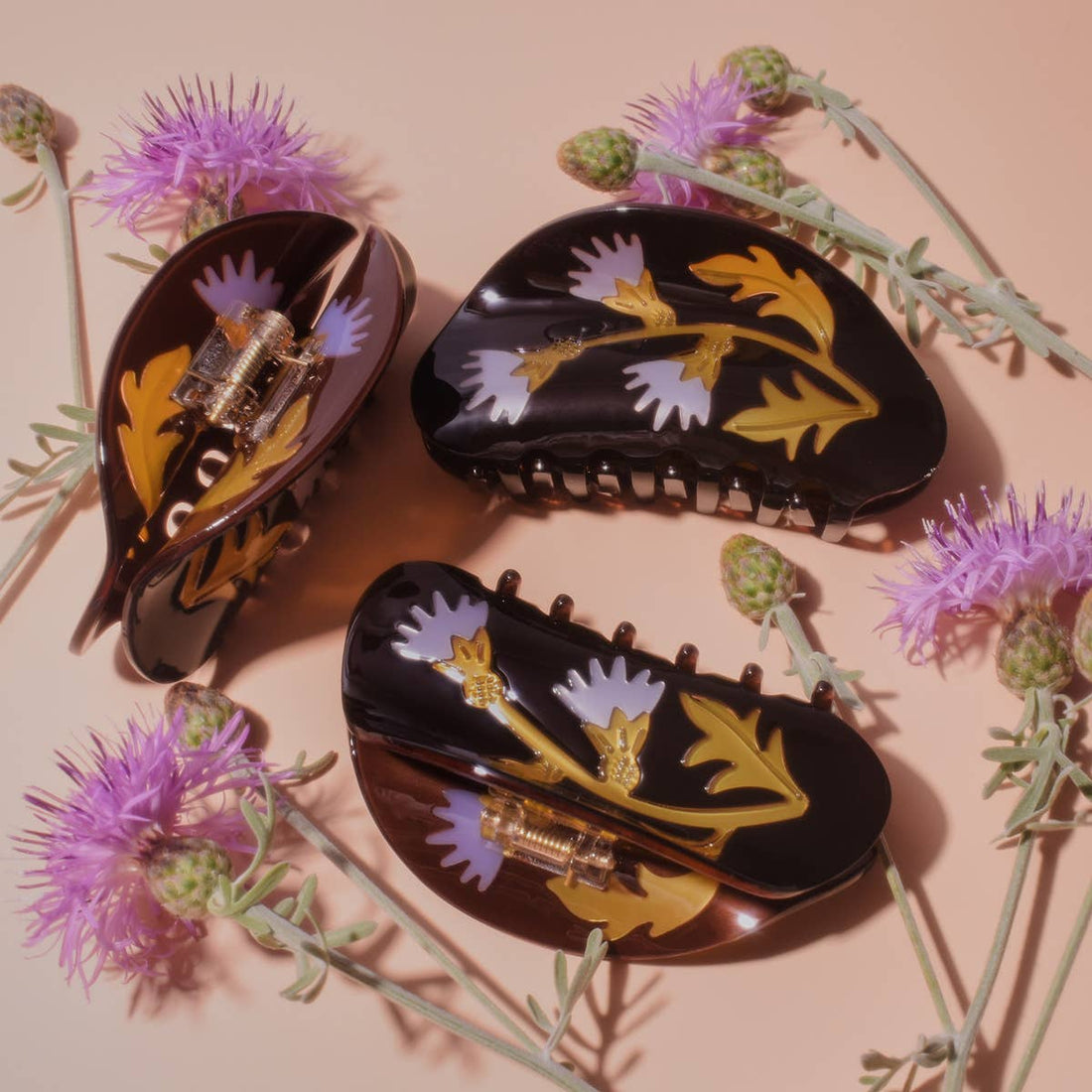 Milk Thistle hair claws, dark brown acetate with purple and gold thistle pattern, one open showing gold spring, flat lay.