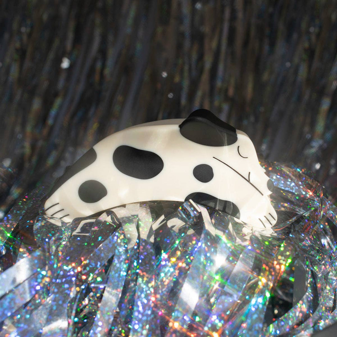 Puppy Claw Spotted Dog hair clip, white and black spotted matte cellulose acetate, side profile resting on iridescent tinsel.