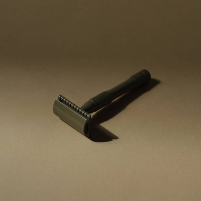 
                    
                      Kelp safety razor, angled close-up showing the textured handle and subtle greenish-grey finish on the brass razor head.
                    
                  