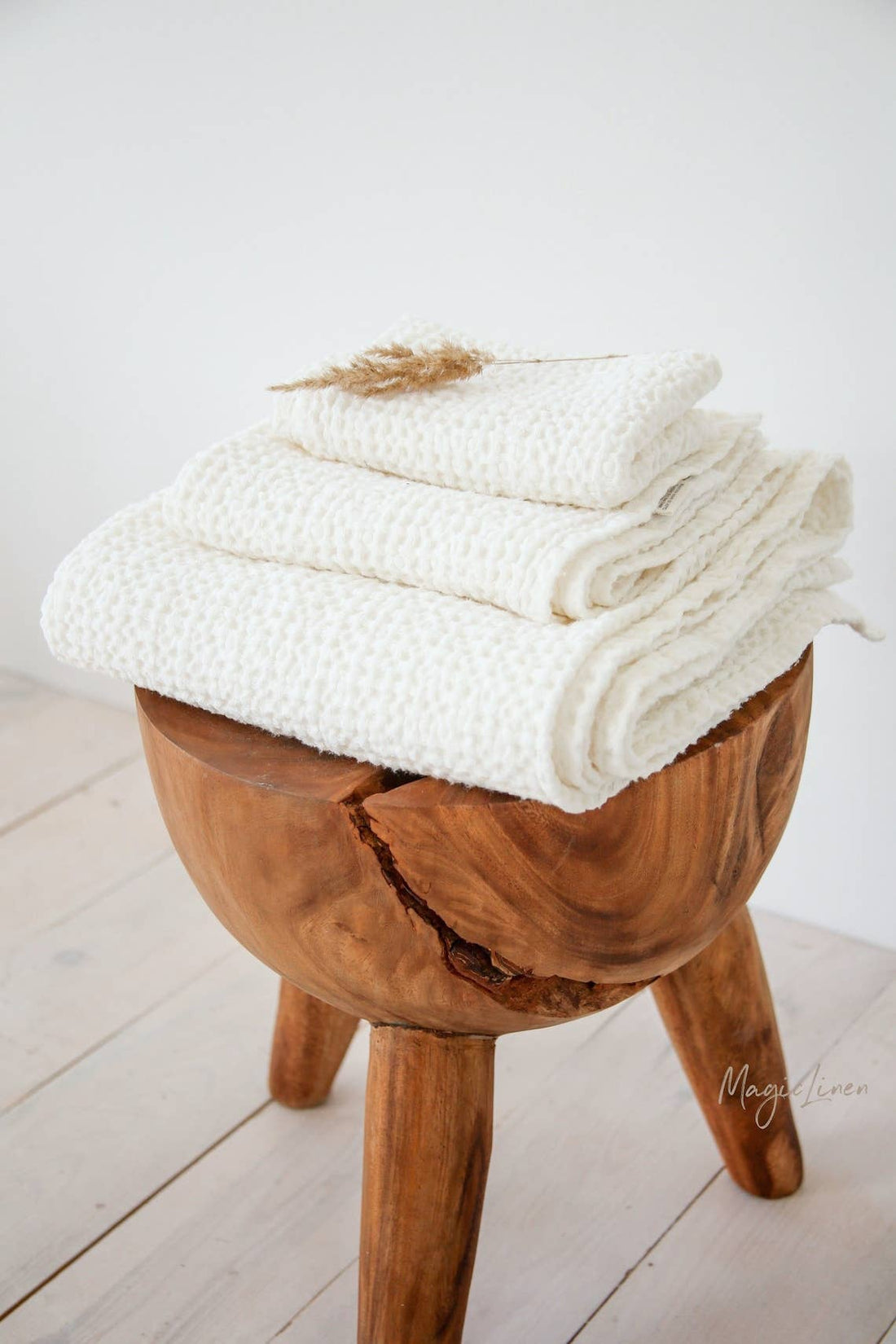 MagicLinen Waffle Linen Bath Towel Set, natural white waffle linen-cotton, stacked on a wooden stool with dried grass.