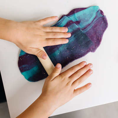 
                    
                      Glitter Natural Play Dough, swirled blue, teal, and purple with sparkling glitter, child's hands rolling with a small wooden…
                    
                  