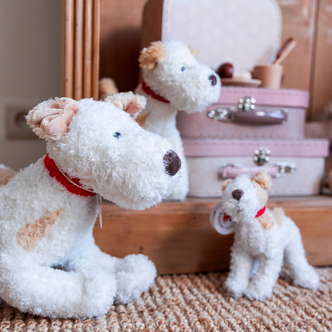 Plush Eliot Stuffed Dogs, white and tan polyester plush, three sizes of dogs with red collars on a woven rug.