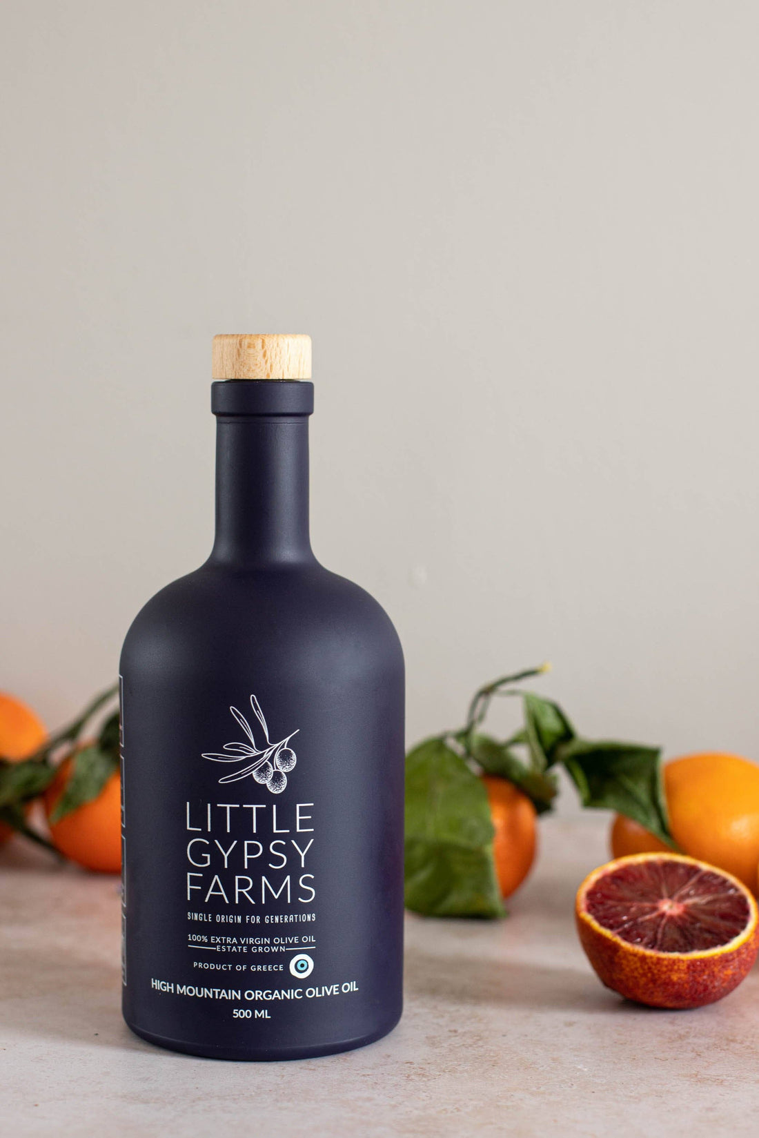Little Gypsy Farms High Mountain Organic Olive Oil, dark blue bottle with cork top, front view surrounded by oranges and…