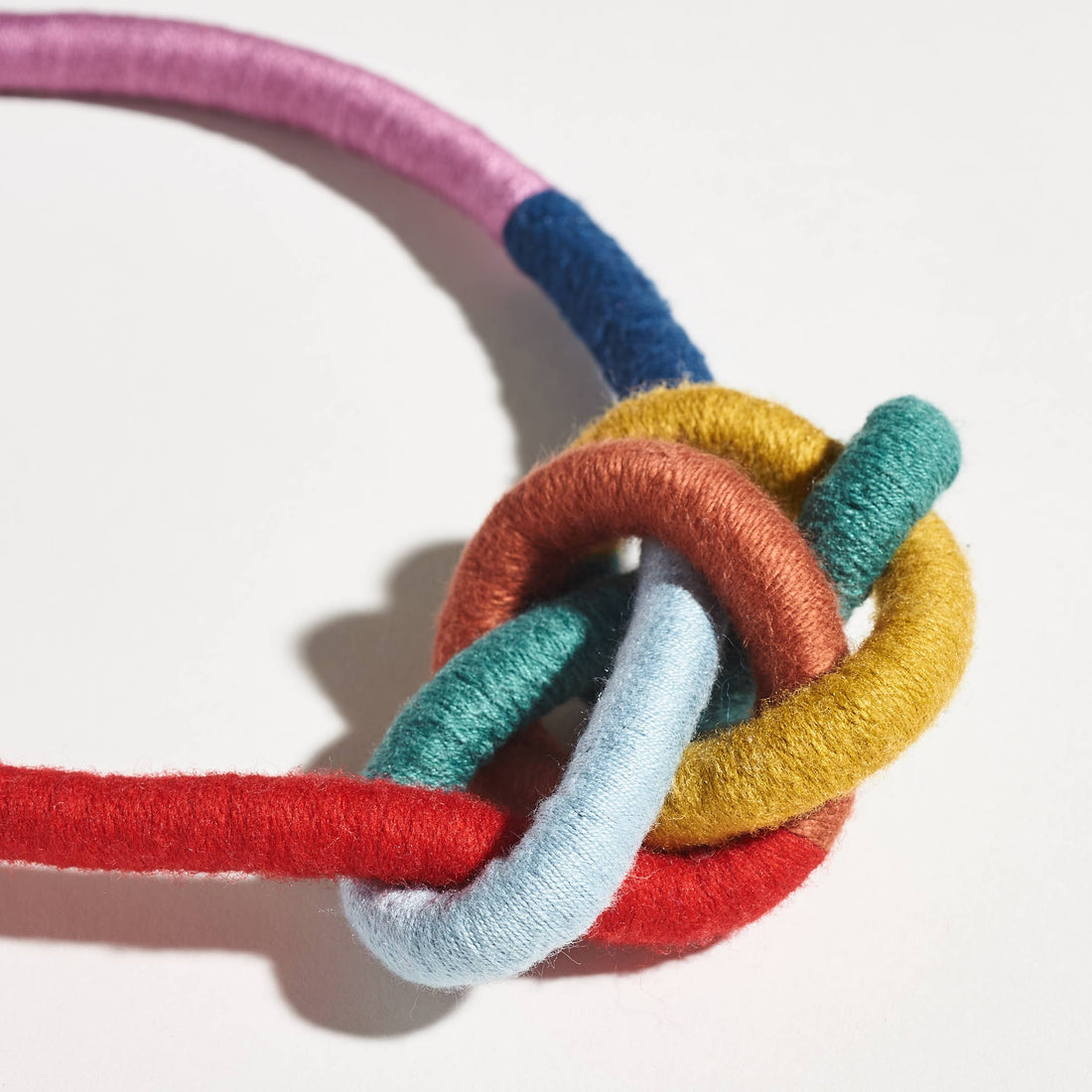 Water Bowline necklace, knot of pink, blue, yellow, red, teal yarn-wrapped cording, close-up detail.