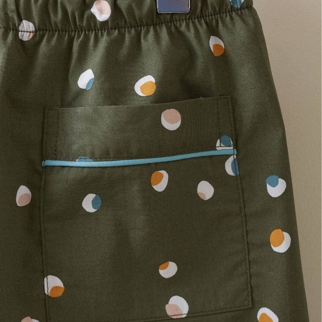 Kids Confetti Pajamas, olive green cotton with white, peach, blue, orange confetti print. Close-up of pocket with blue…