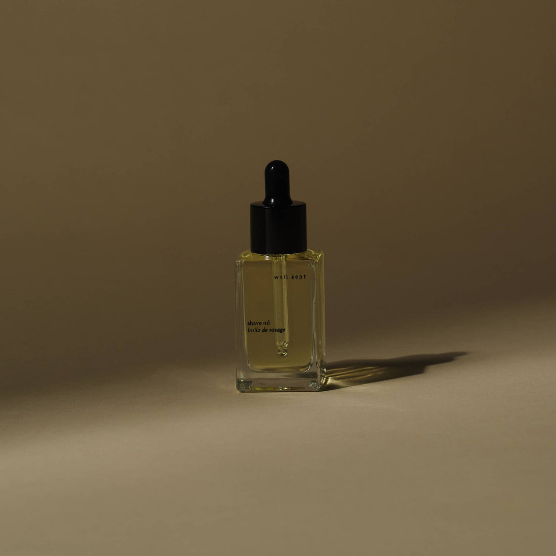Shave oil, light golden liquid in clear glass dropper bottle, front-angled view showing internal dropper.