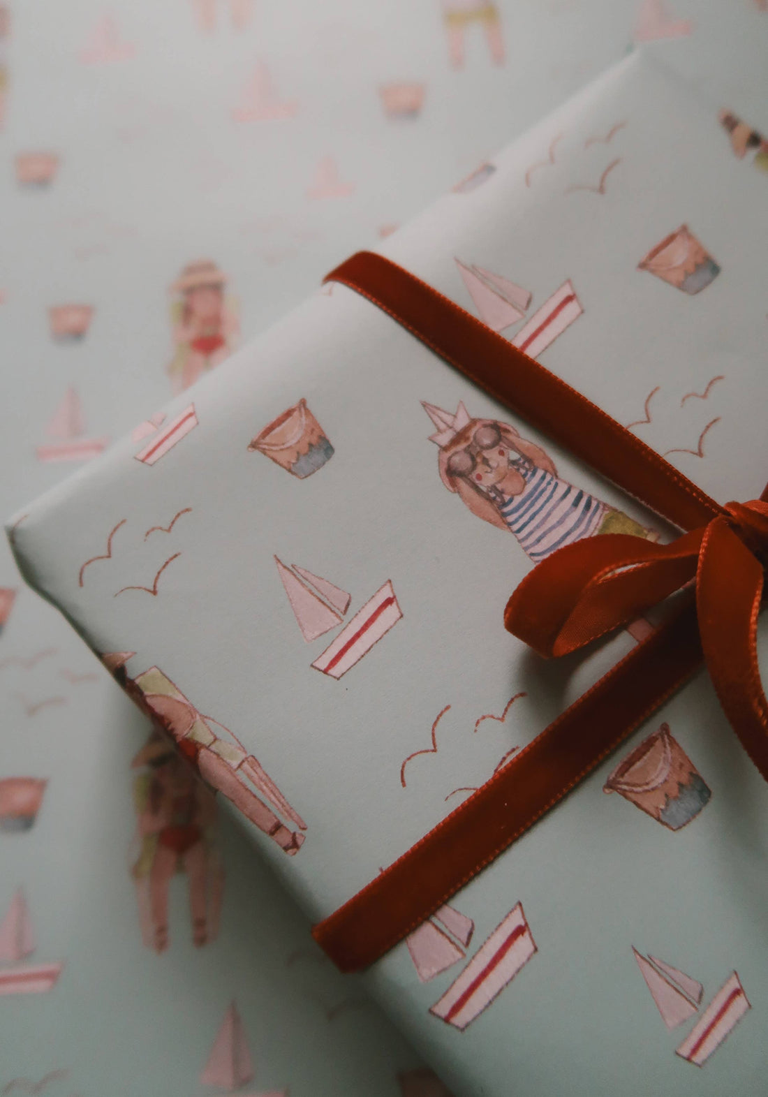 Summer Wrapping Paper, light blue with watercolor illustrations of swimmers, sailboats, buckets. Wrapped gift detail with…