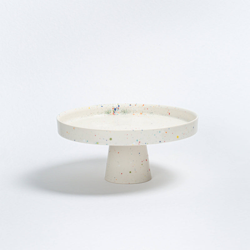 Egg Back Home Confetti Glaze stoneware cake stand, off-white with colorful speckles, front view on white.