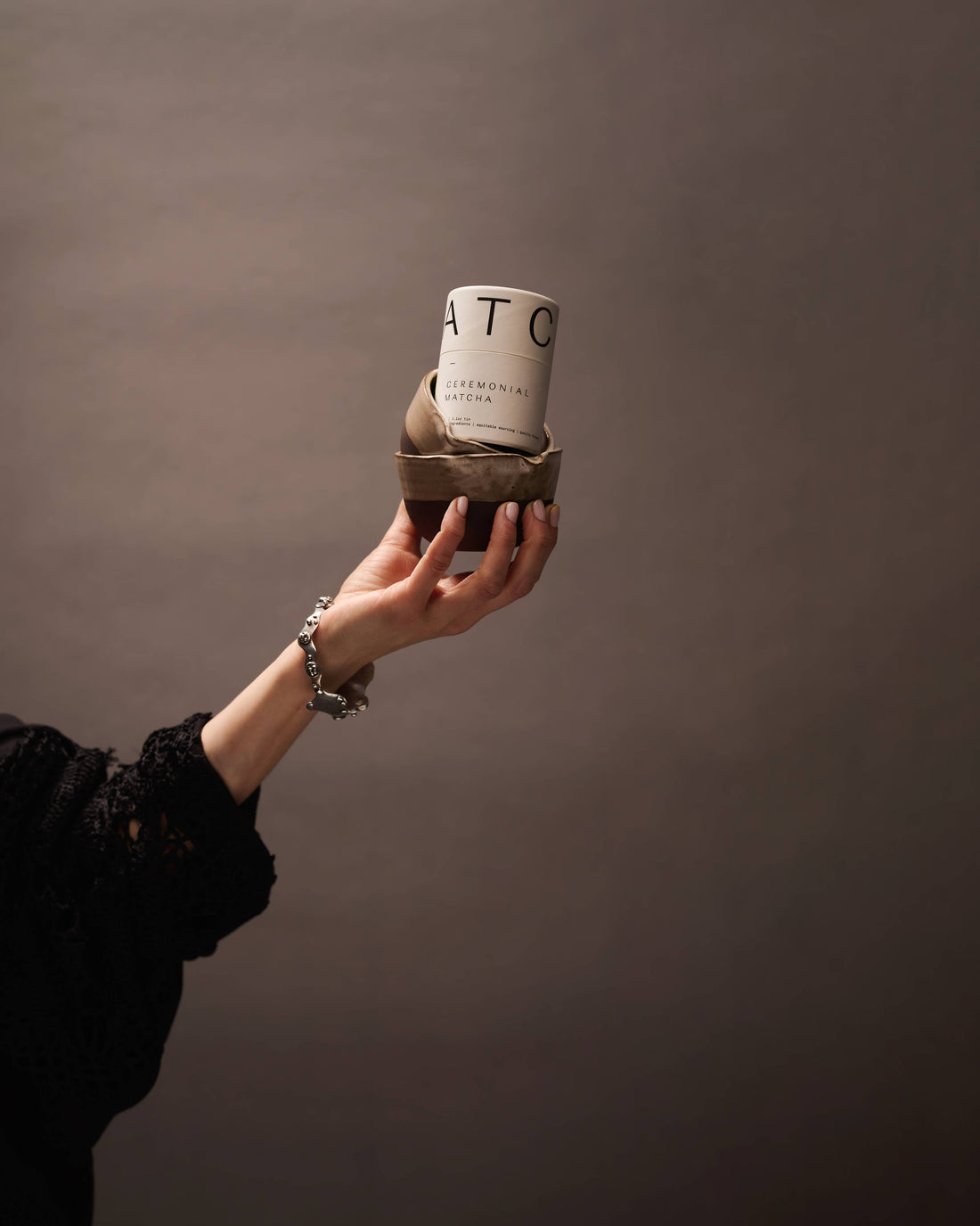 Ceremonial Matcha white tin with black text, sitting in a two-toned brown ceramic bowl, held by a hand for scale.
