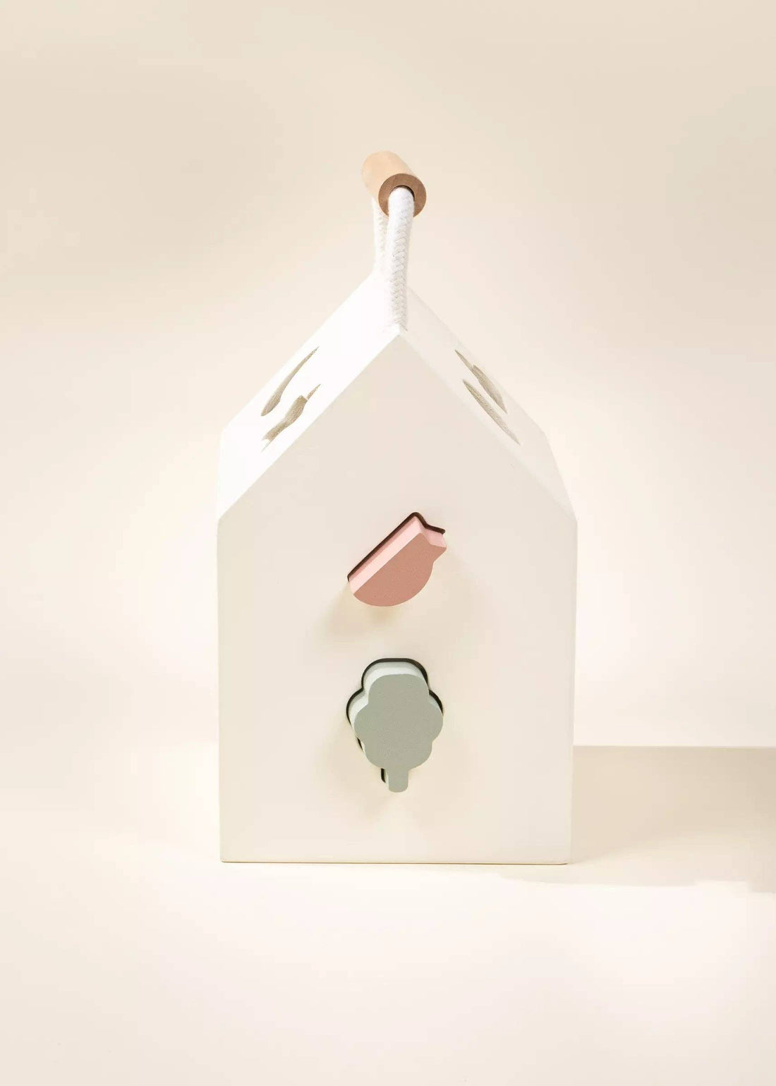 Wooden Shapes Sorting House, white wood, pink bird & sage tree shapes, natural wood & rope handle; angled side view.