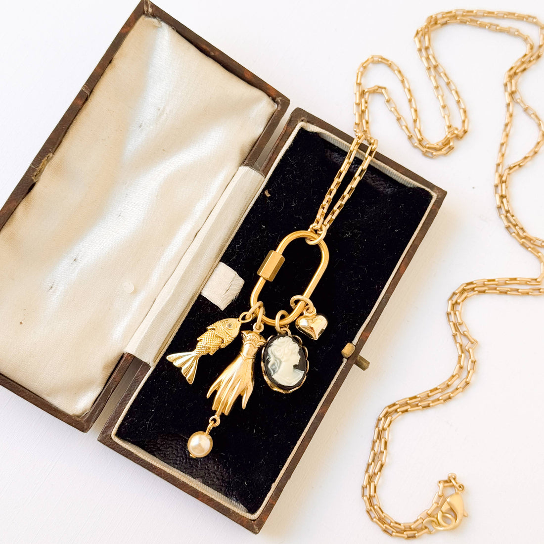 Close-up of Gold Carabiner Charm Necklace with varied charms and pearl, resting in an open velvet box.
