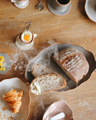 
                    
                      Handcrafted Stoneware Tray, grey speckled glaze, organic wavy rim, overhead view with fresh sliced bread and breakfast items.
                    
                  
