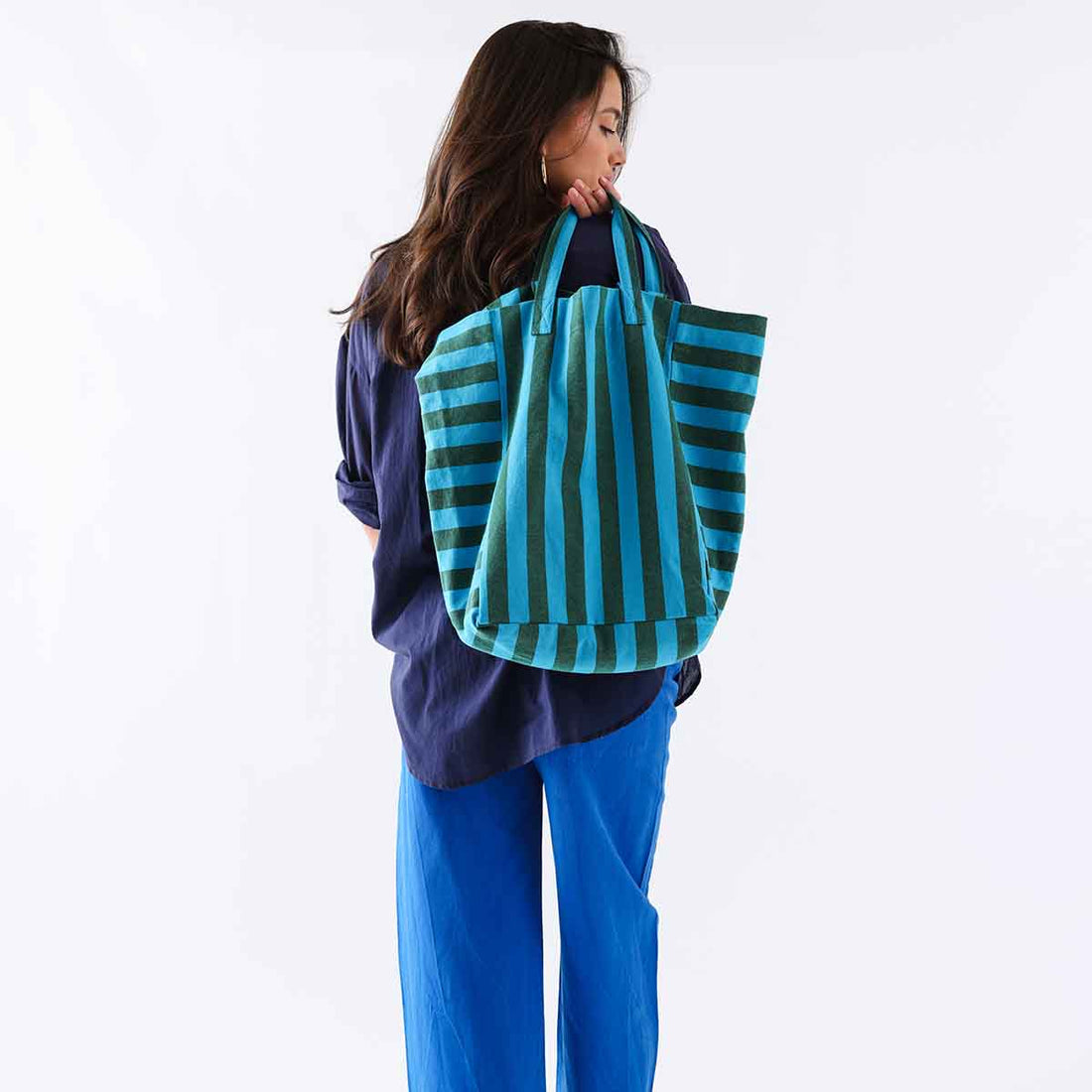 Elisabeth cotton tote bag with turquoise and olive green vertical stripes, worn over model's shoulder, back view.