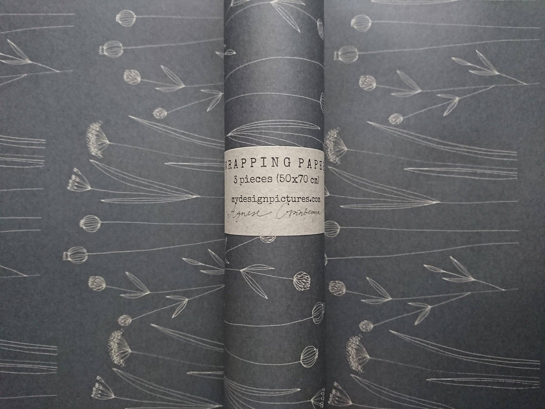 Botanical wrapping paper, dark gray kraft with white floral pattern, rolled sheet with product label, flat background.