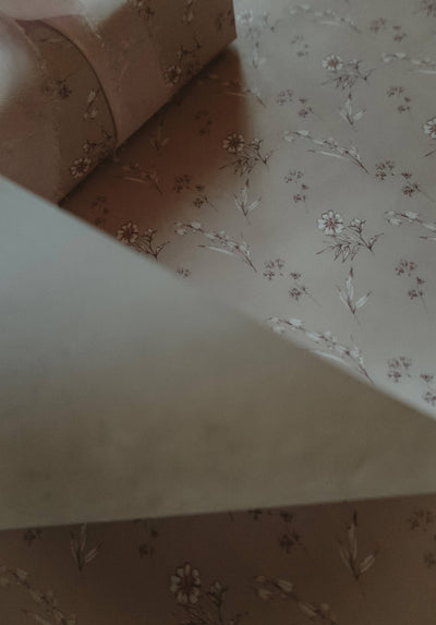 
                    
                      Vintage Blooms wrapping paper, Agnese Grīnberga's delicate floral illustration on light brown, partially rolled detail view.
                    
                  
