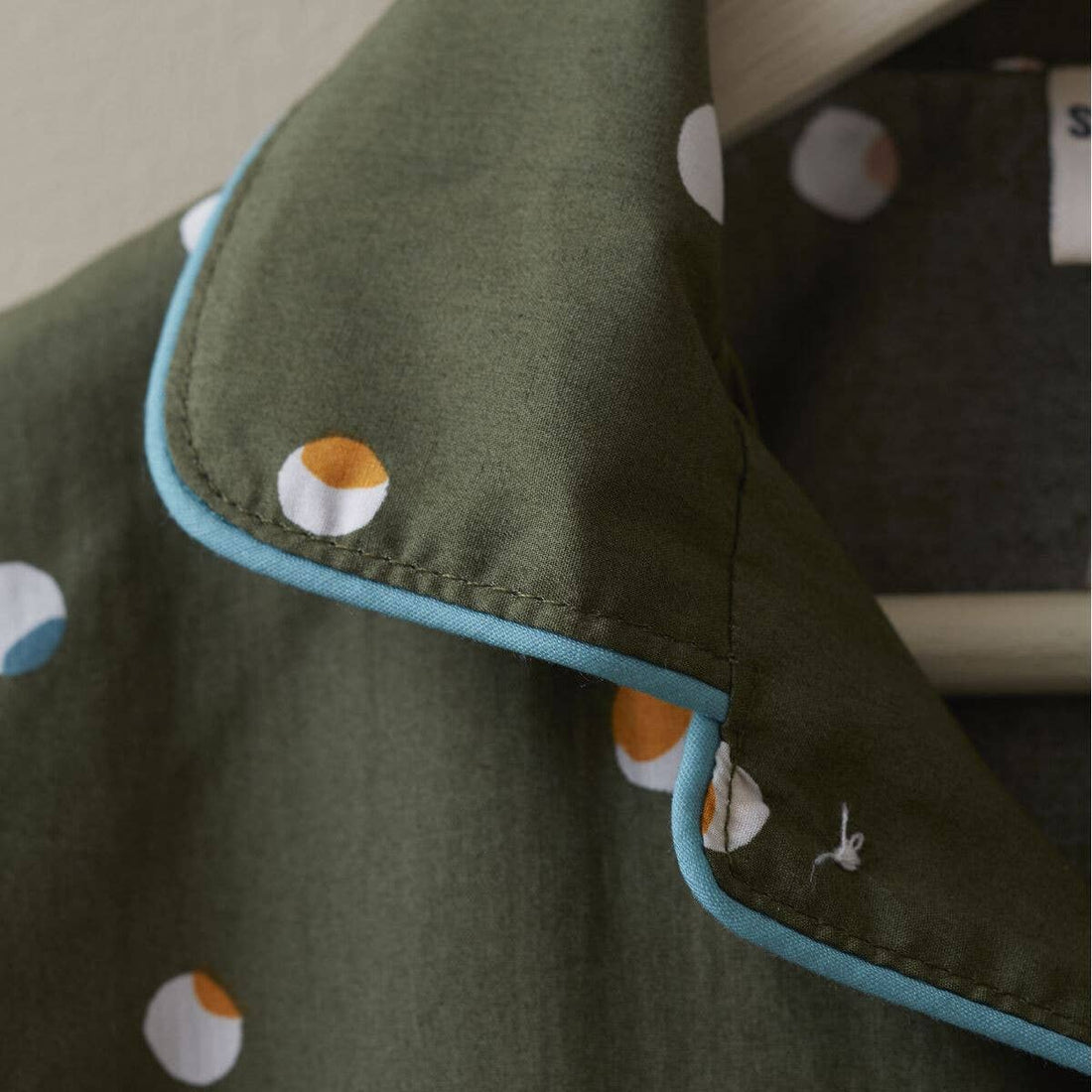 Confetti Kids Pajamas, olive green cotton collar, close-up view of white and orange confetti dots, light blue piping.